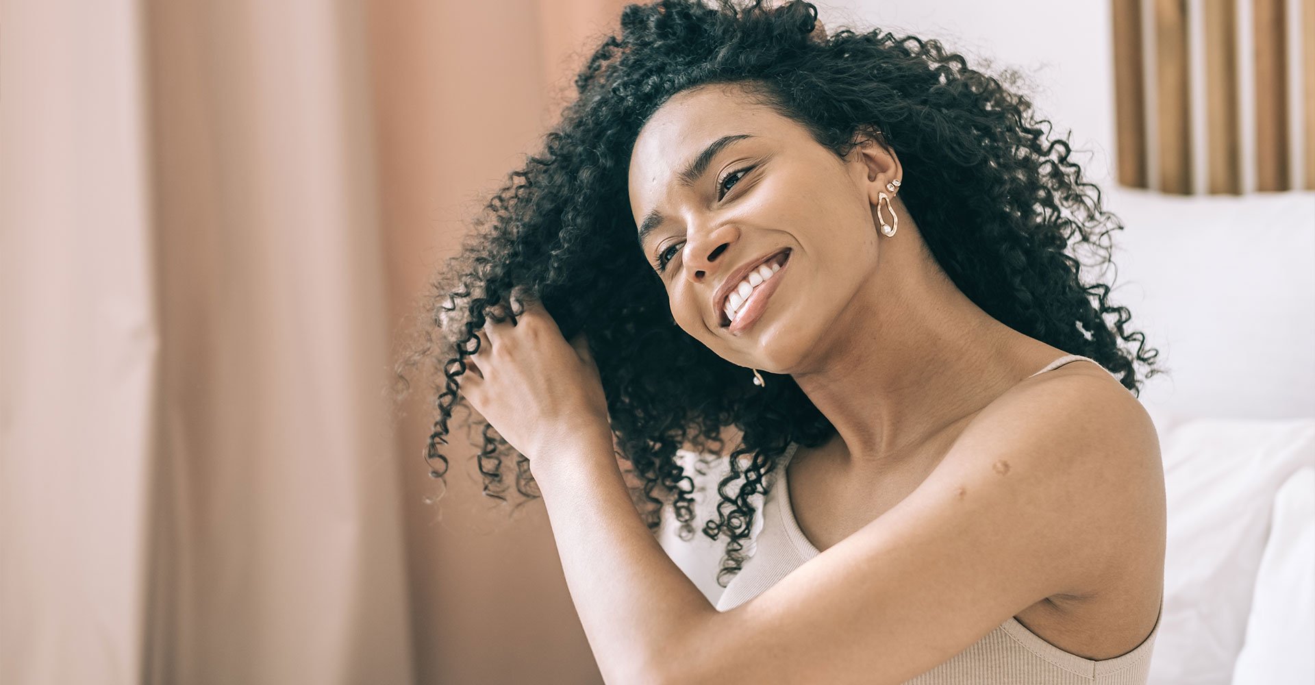 Mulher negra sorri ao tocar os cachos definidos, possivelmente com dedoliss, em seu cabelo